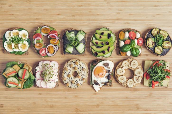 Gluten-free bread & bagels with 12 appetizing toppings like avocado & olives, hummus & chickpeas, sliced hardboiled eggs & greens; concept is celiac disease